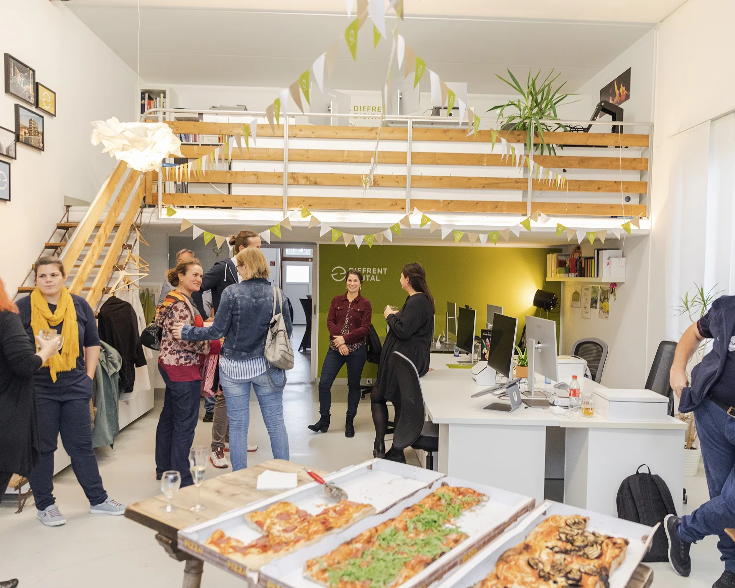 Gäste im Atelier um lange Tische mit Flammkuchen, dahinter die Galerie mit Holzgeländer