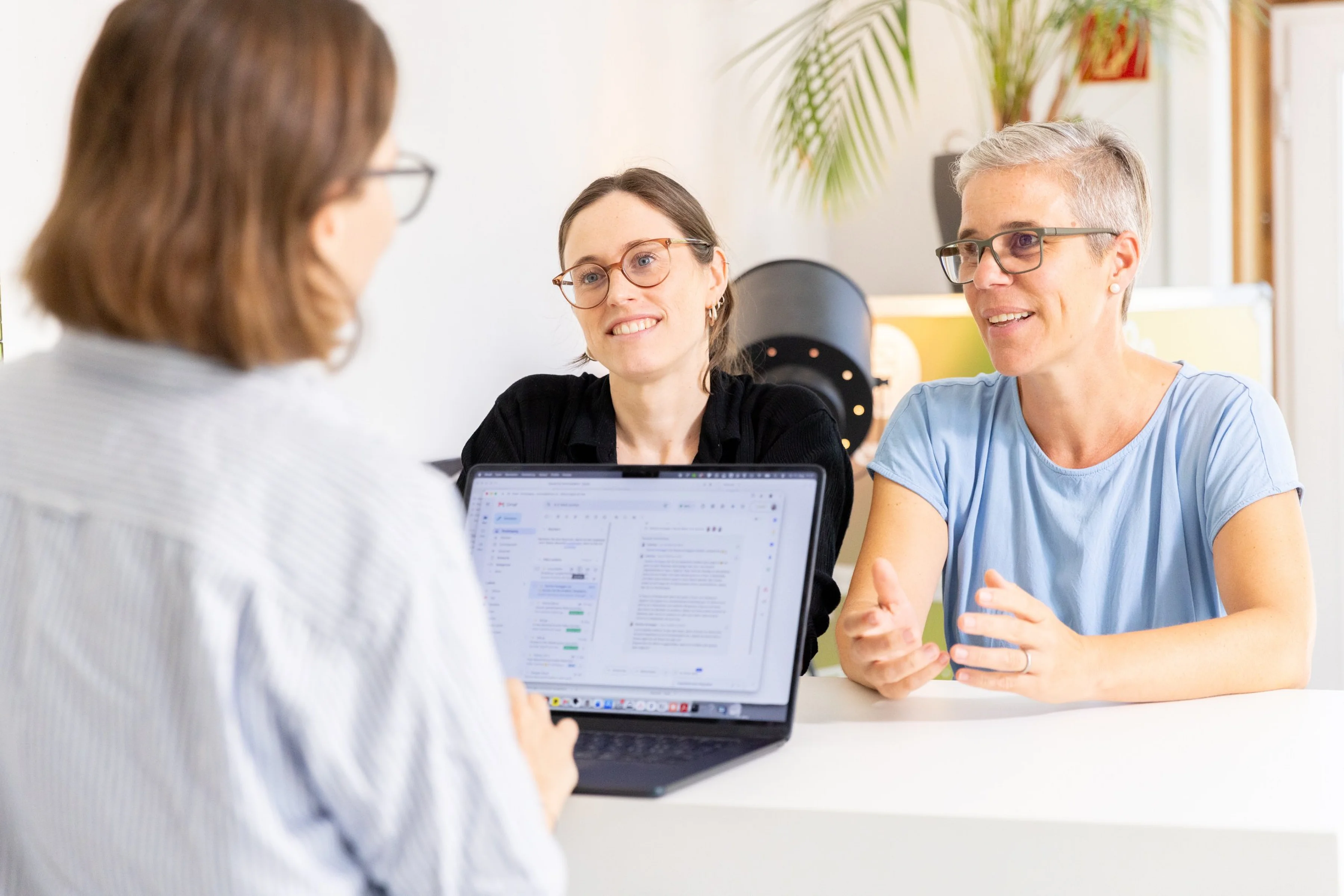 Drei Frauen im Gespräch am Besprechungstisch, dazwischen ein aufgeklappter Laptop