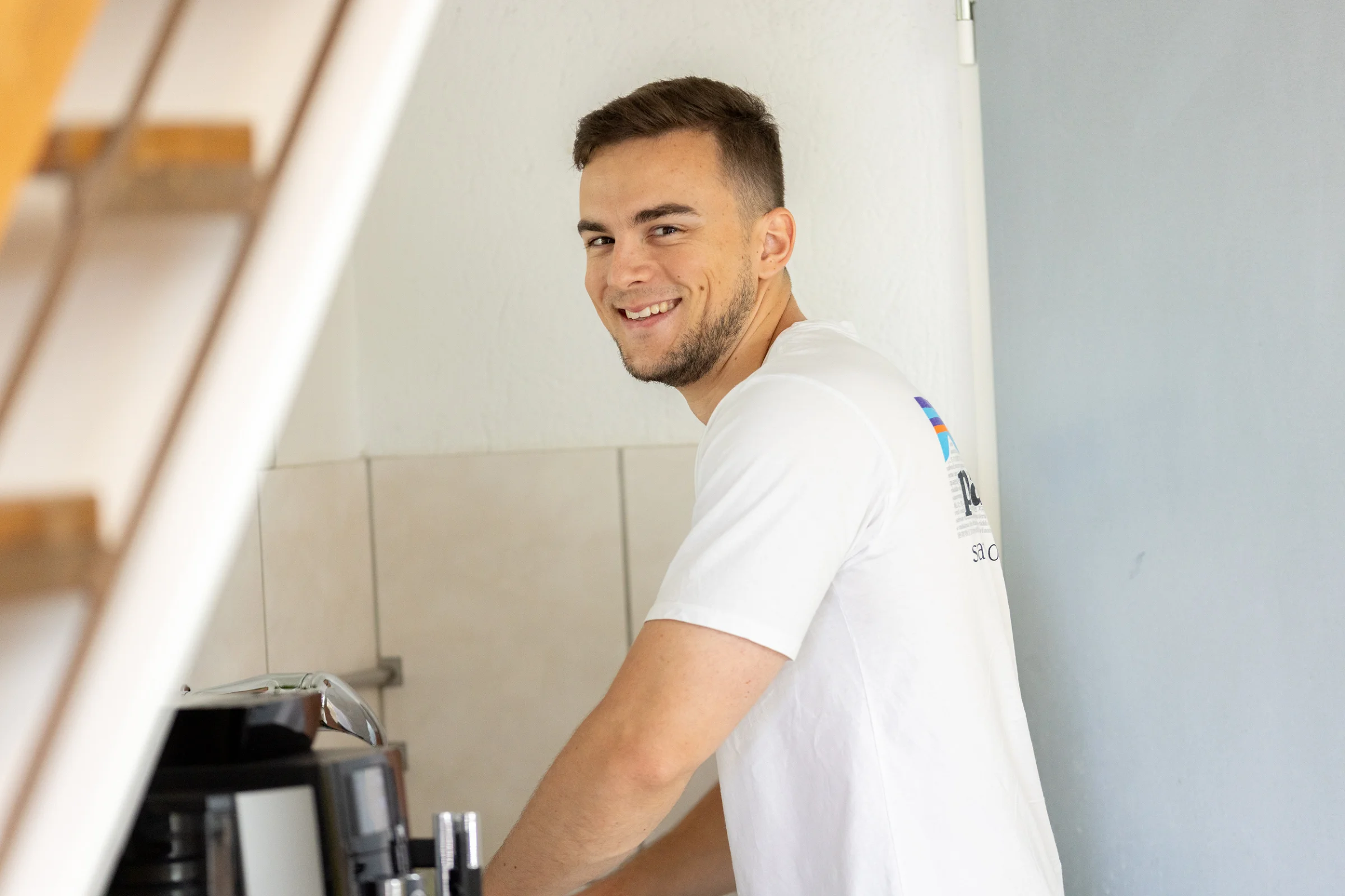 Pascal lächelt über die Schulter, während er sich einen Kaffee macht
