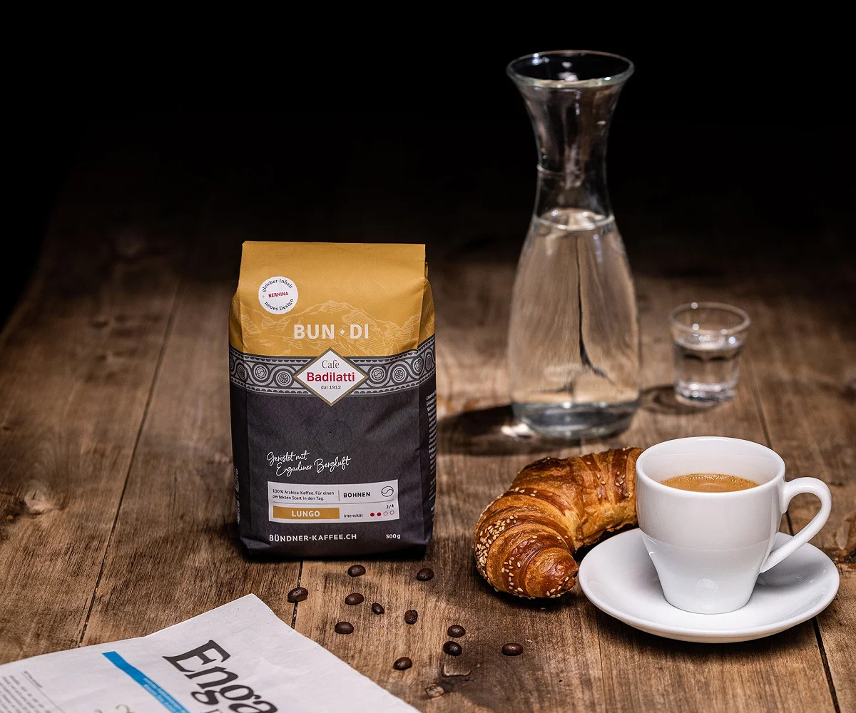 Kaffeepackung «Bun·Di» neben Karaffe, Gipfeli und Tasse auf einem Holztisch