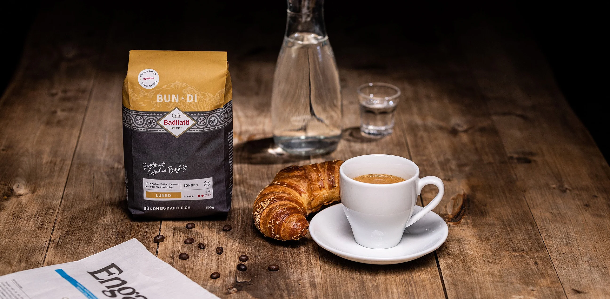 Kaffeepackung «Bun·Di» neben Karaffe, Gipfeli und Tasse auf einem Holztisch