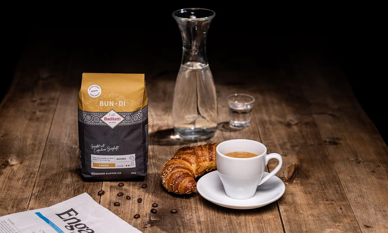 Kaffeepackung «Bun·Di» neben Karaffe, Gipfeli und Tasse auf einem Holztisch