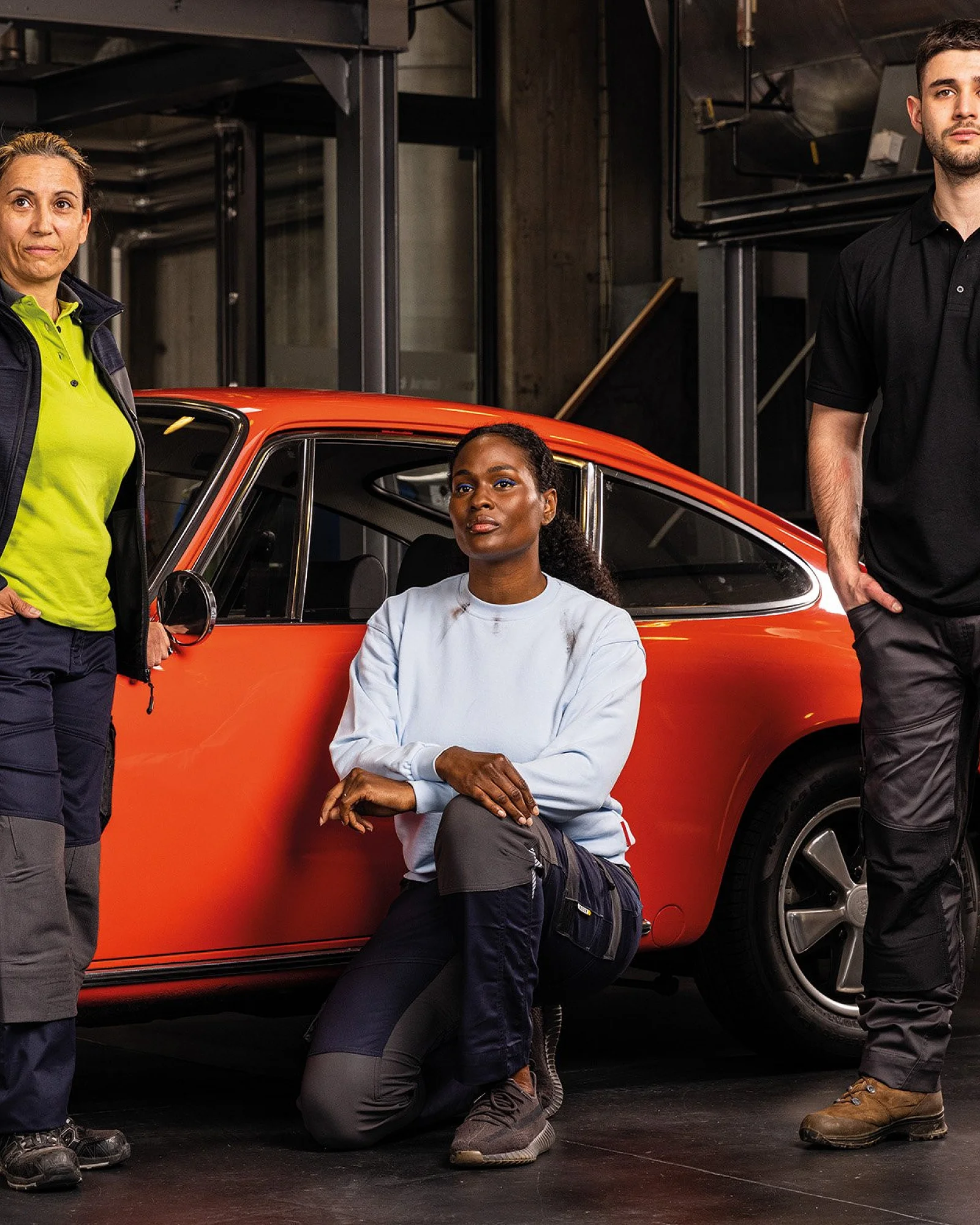 Drei Personen in Arbeitskleidung vor einem roten Oldtimer in der Werkstatt