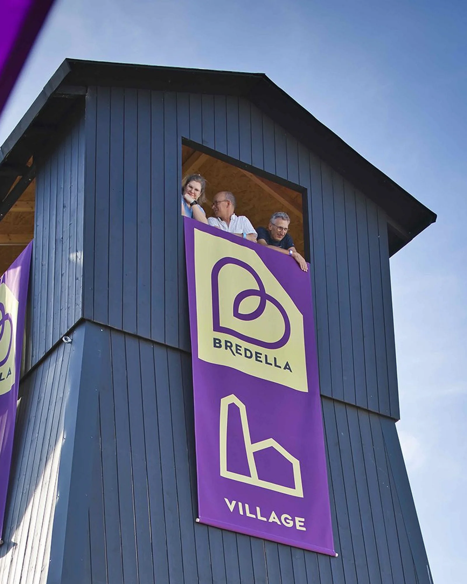Salzbohrturm des Bredella Village mit den Bannern «Bredella» und «Village», drei Menschen schauen aus der Turmöffnung. Foto Marc Gilgen