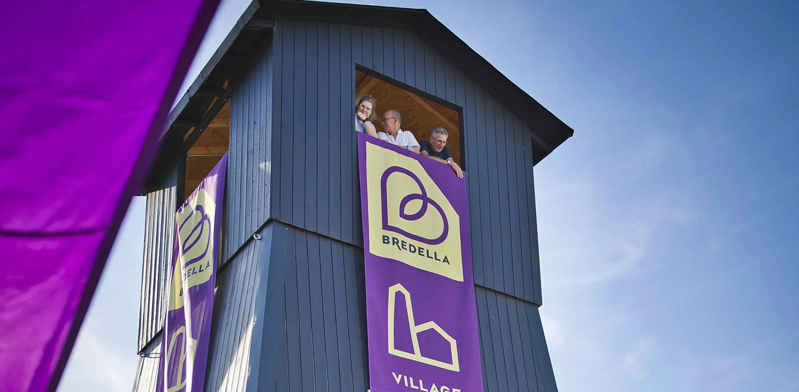 Salzbohrturm des Bredella Village mit den Bannern «Bredella» und «Village», drei Menschen schauen aus der Turmöffnung. Foto Marc Gilgen
