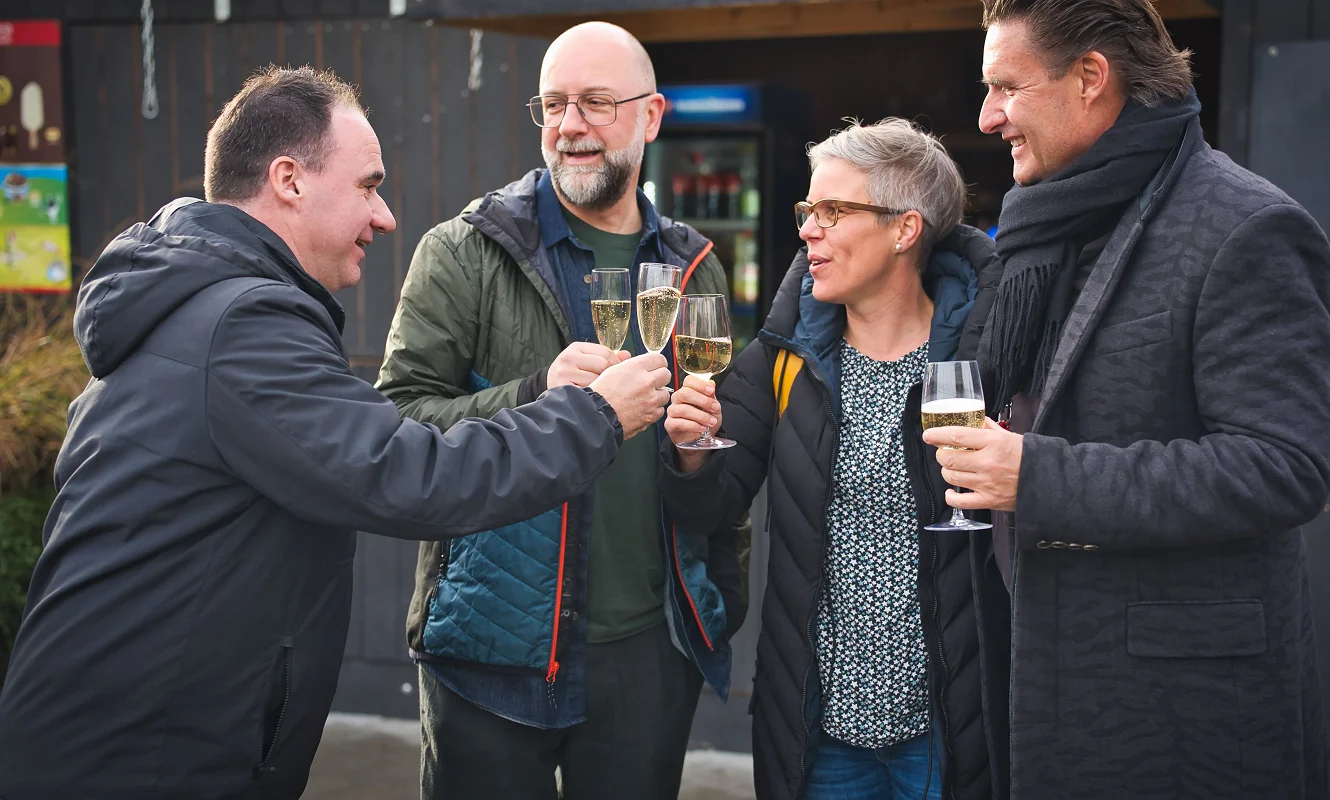 Vier Menschen stossen mit Gläsern vor dem Pavillon des Bredella Village an. Foto Marc Gilgen