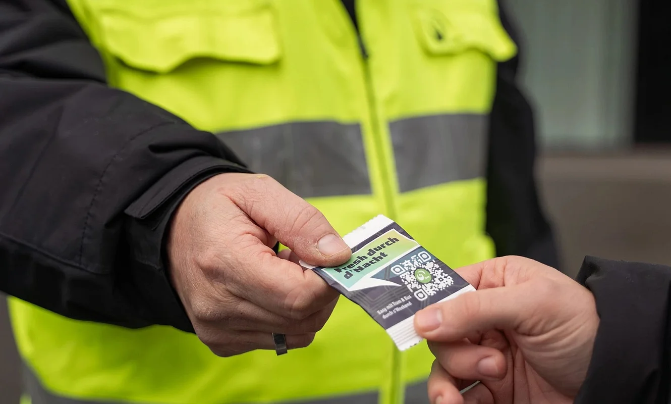 Ein Kampagnenkärtchen mit QR-Code wird von Hand zu Hand weitergegeben