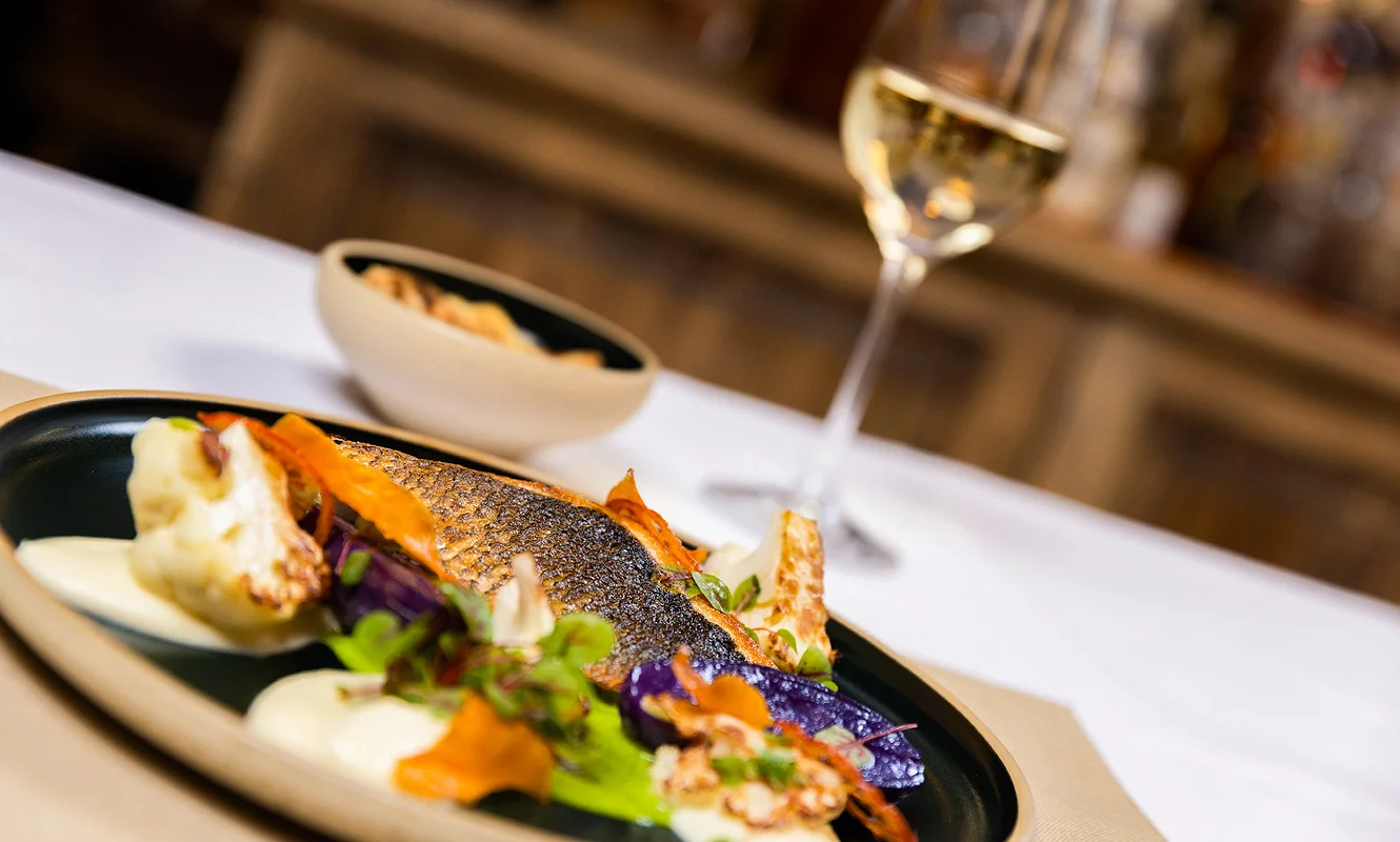 Gebratenes Fischfilet mit Blumenkohl, Rüebli und Kresse auf dunklem Teller