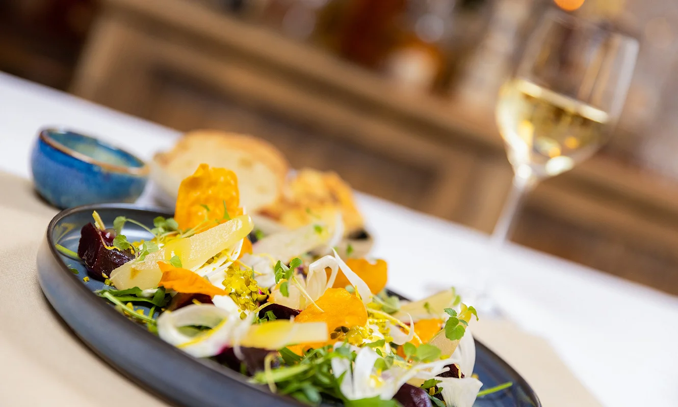 Randensalat mit Fenchel, Orange und Kresse auf dunklem Teller, dahinter ein Glas Weißwein