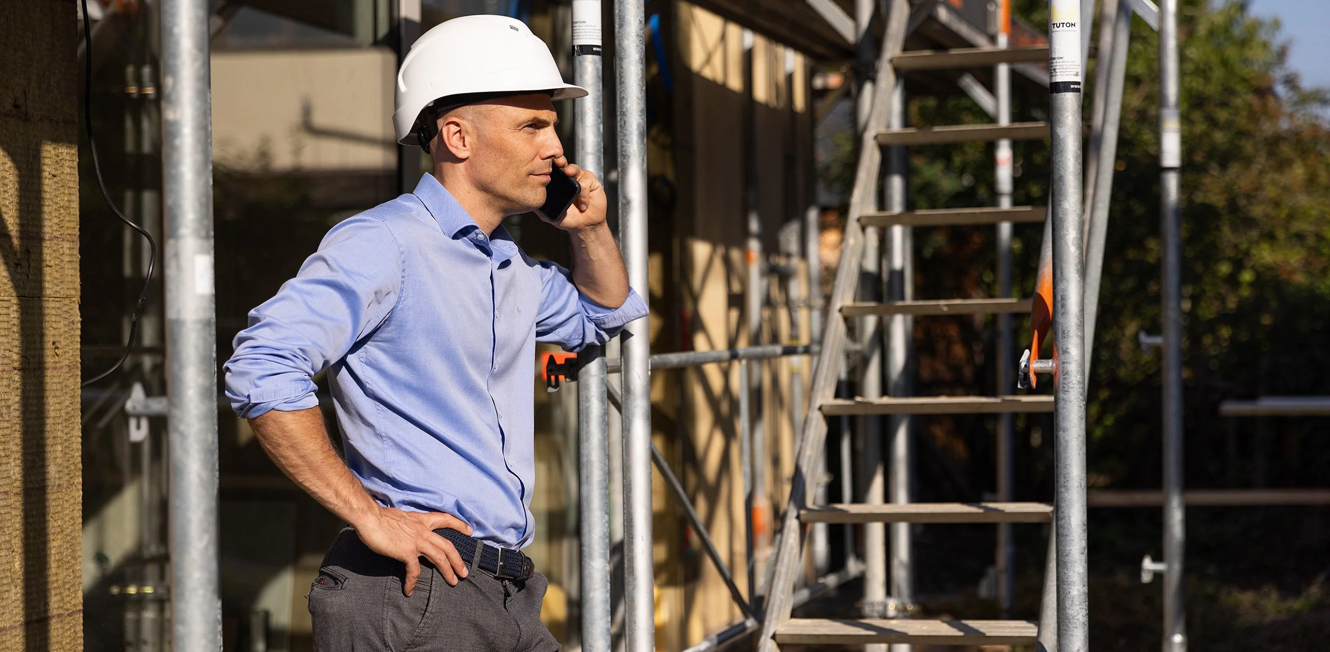 Person mit weißem Helm telefoniert auf einer Baustelle neben dem Gerüst