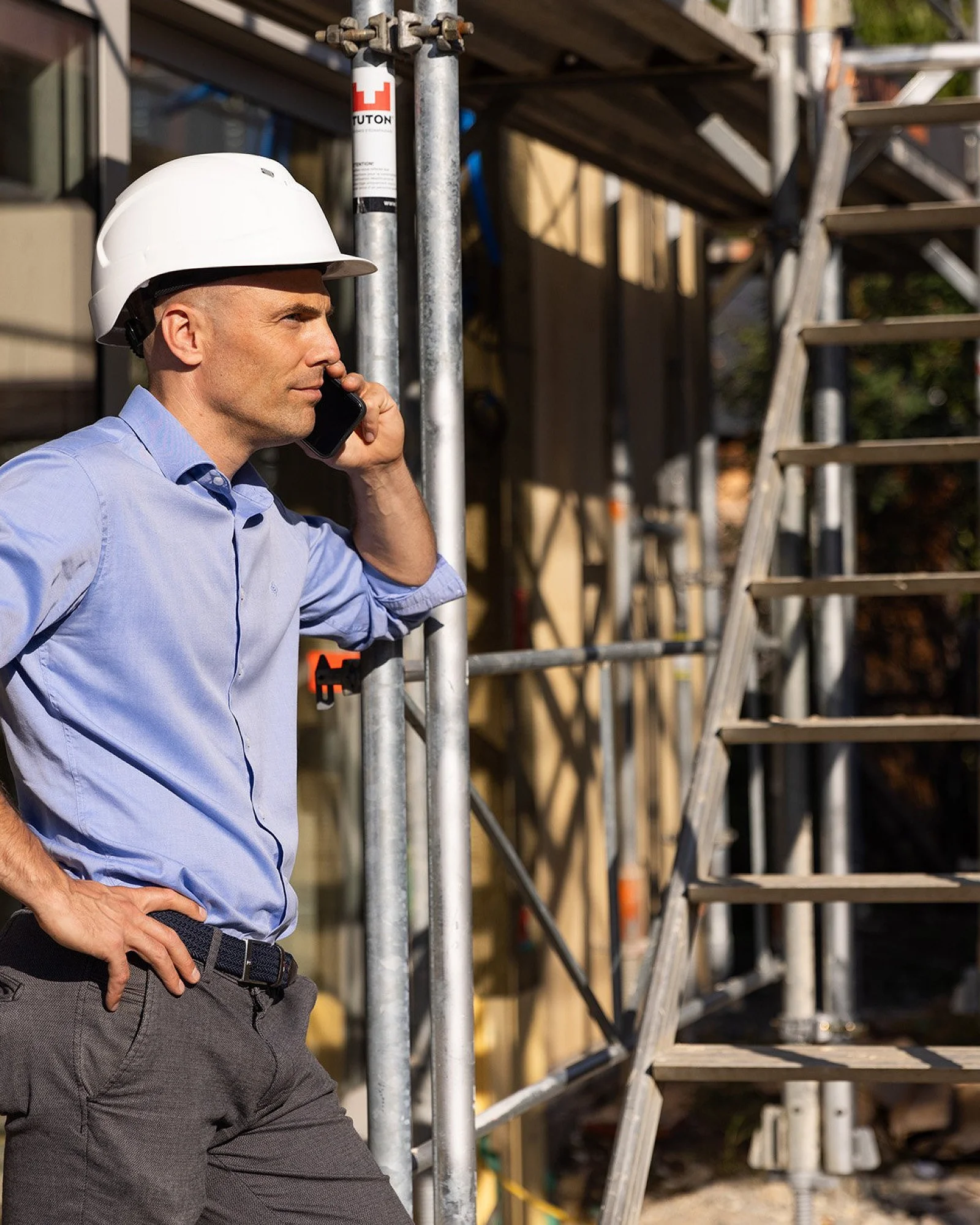 Person mit weißem Helm telefoniert auf einer Baustelle neben dem Gerüst