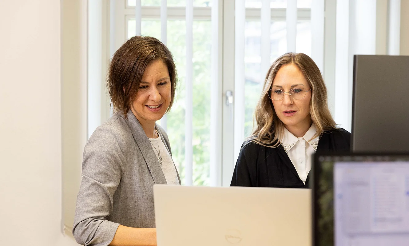 Zwei Personen schauen gemeinsam auf einen Laptop im hellen Büro