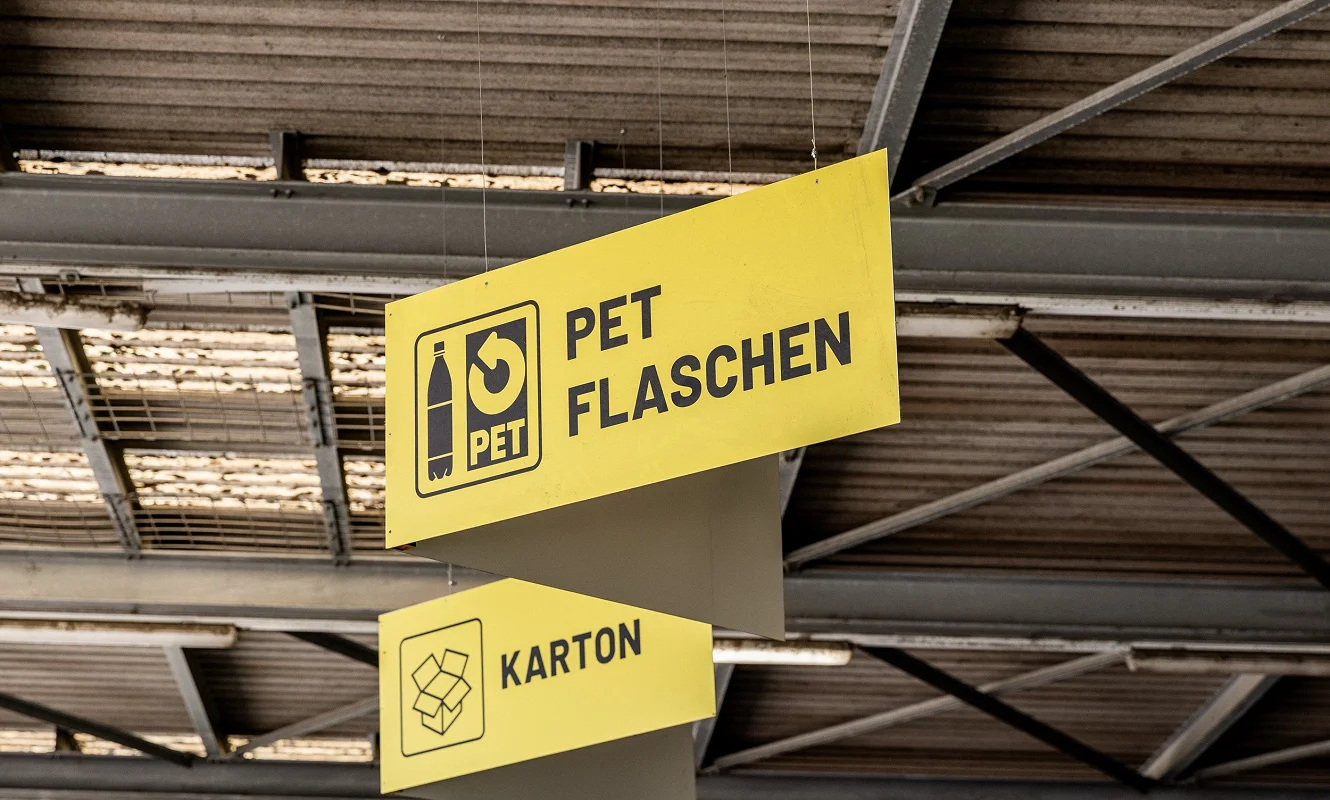 Abgehängte Schilder in der Halle: «PET Flaschen» und «Karton» mit Piktogrammen