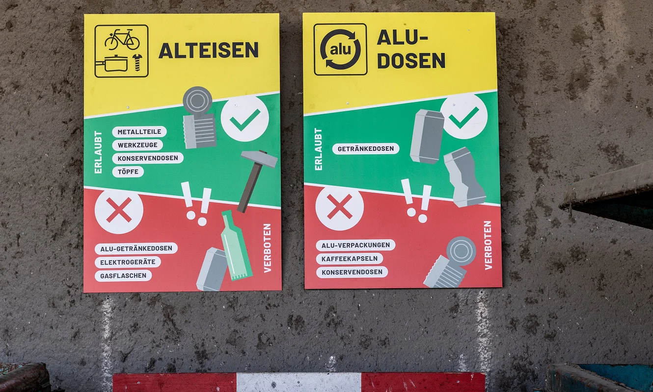 Zwei Tafeln an der Betonwand: «Alteisen» und «Alu-Dosen», je mit grüner Erlaubt- und roter Verboten-Liste
