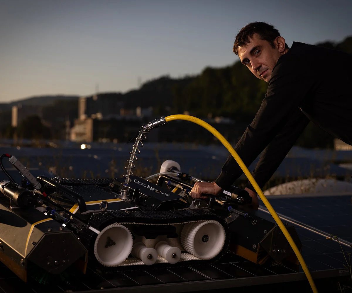 Reinigungsroboter auf einer Photovoltaikanlage, daneben eine Person mit Wasserschlauch in der Dämmerung